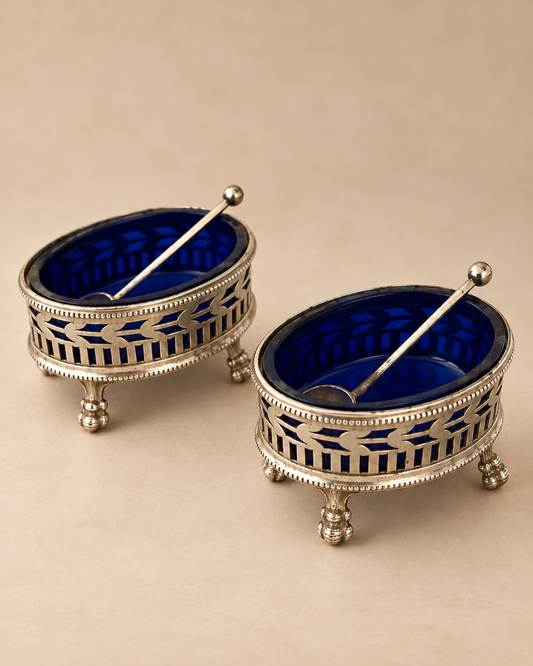 Pair of pierced silver salt cellars with beaded rims, ball feet and cobalt blue glass liners, angled view