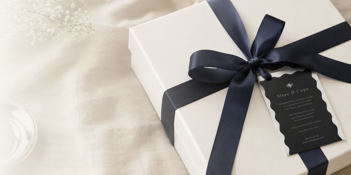 A wrapped More & Cope gift box with a navy ribbon, cream fabric, flowers, and silver accents, styled for thoughtful wedding and home gifting