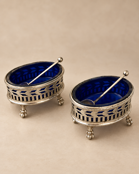 Pair of antique J.M. van Kempen Dutch silver salt cellars with cobalt glass liners and spoons, angled view on warm beige